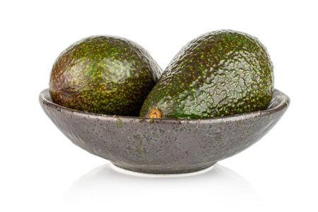 Group of two whole fresh green avocado in dark ceramic bowl isolated on white backgroundの写真素材