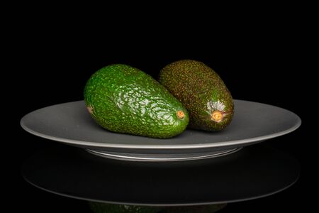 Group of two whole fresh green avocado on gray ceramic plate isolated on black glassの写真素材