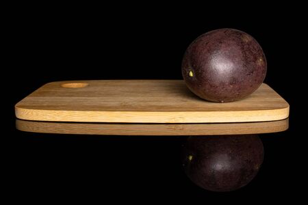 One whole sweet dark purple passion fruit on bamboo cutting board isolated on black glassの写真素材
