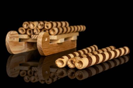 Lot of whole crunchy beige hazelnut rolled wafer biscuit with wooden sledge isolated on black glass