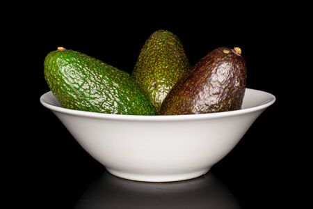 Group of three whole fresh green avocado in white ceramic bowl isolated on black glassの写真素材