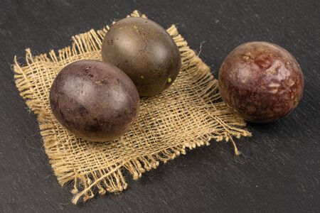Group of three whole sweet dark purple passion fruit on natural sackcloth on grey stoneの写真素材