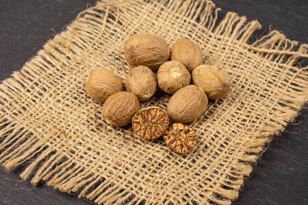 Group of eight whole one half one piece of dry brown nutmeg on natural sackcloth on grey stone