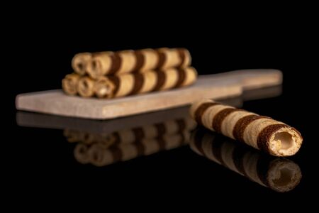 Group of six whole crunchy beige hazelnut rolled wafer biscuit on small wooden cutting board isolated on black glassの写真素材