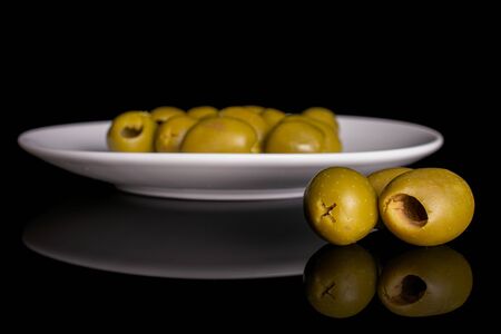 Lot of whole pitted green olive on white ceramic plate isolated on black glassの写真素材