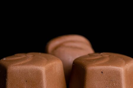 Group of three whole delicious chocolate praline in closeup isolated on black glass
