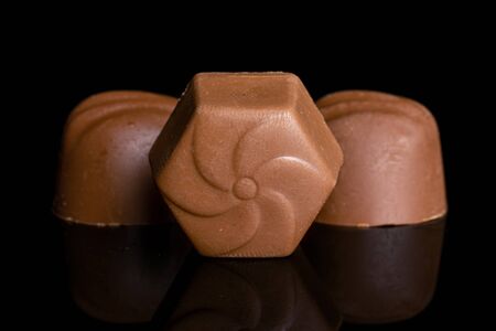 Group of three whole light brown delicious chocolate praline isolated on black glass