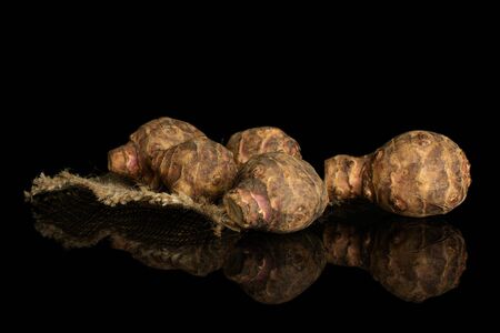 Group of five whole fresh brown jerusalem artichoke on natural sackcloth isolated on black glassの写真素材