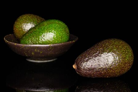 Group of three whole fresh green avocado in dark ceramic bowl isolated on black glassの写真素材
