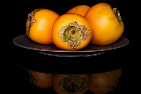 Group of four whole sweet orange persimmon on gray ceramic plate isolated on black glassの写真素材