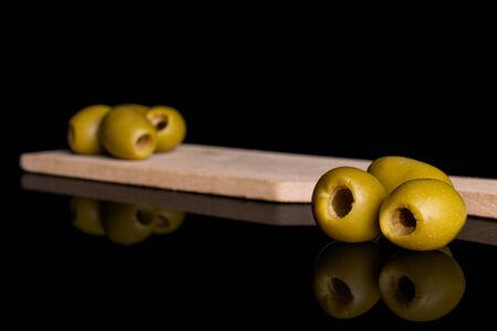 Group of six whole pitted green olive on small wooden cutting board isolated on black glassの写真素材