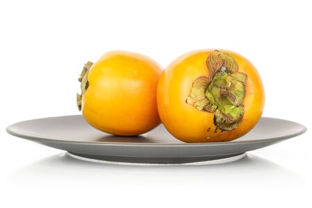 Group of two whole sweet orange persimmon on gray ceramic plate isolated on white backgroundの写真素材