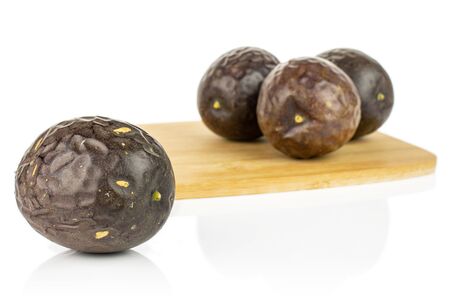 Group of four whole sweet dark purple passion fruit on bamboo cutting board isolated on white backgroundの写真素材