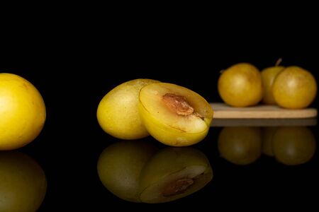 Group of four whole two halves of fresh yellow plum on bamboo cutting board isolated on black glassの写真素材
