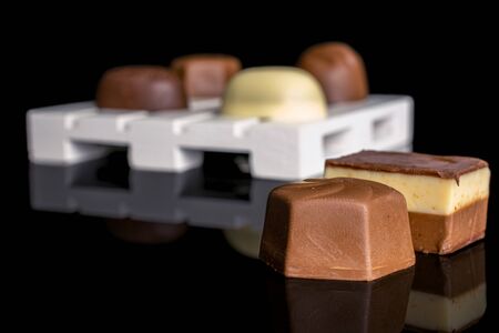 Group of six whole delicious chocolate praline on white wooden pallet isolated on black glass