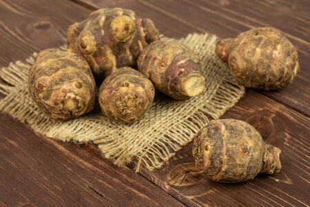Group of six whole fresh brown jerusalem artichoke on natural sackcloth on brown woodの写真素材