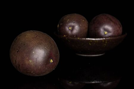 Group of three whole sweet dark purple passion fruit in dark ceramic bowl isolated on black glassの写真素材
