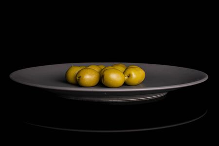 Lot of whole pitted green olive on gray ceramic plate isolated on black glassの写真素材