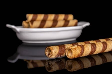 Group of five whole crunchy beige hazelnut rolled wafer biscuit in white oval ceramic bowl isolated on black glassの写真素材