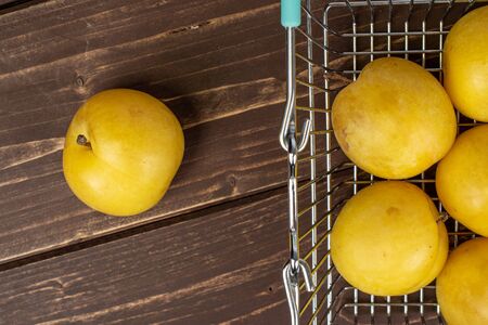 Group of six whole fresh yellow plum in shopping basket flatlay on brown woodの写真素材