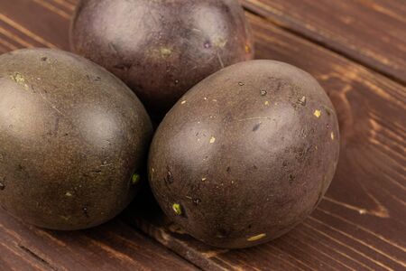 Group of three whole sweet dark purple passion fruit on brown woodの写真素材
