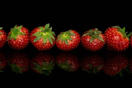 Group of six whole fresh red strawberry line isolated on black glassの写真素材