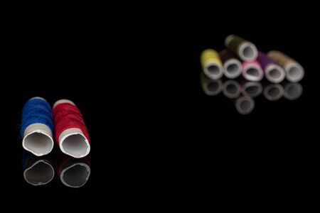 Group of eight whole sewing thread spool two in focus isolated on black glass