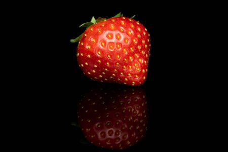 One whole fresh red strawberry isolated on black glassの写真素材