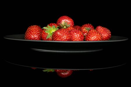 Lot of whole fresh red strawberry heap on gray ceramic plate isolated on black glassの写真素材