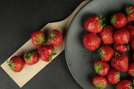 Lot of whole fresh red strawberry on gray ceramic plate on wooden cutting board flatlay on grey...