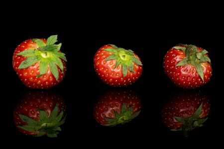 Group of three whole fresh red strawberry isolated on black glassの写真素材