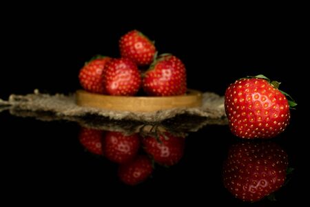 Group of five whole fresh red strawberry on round bamboo coaster with jute fabric isolated on black glassの写真素材