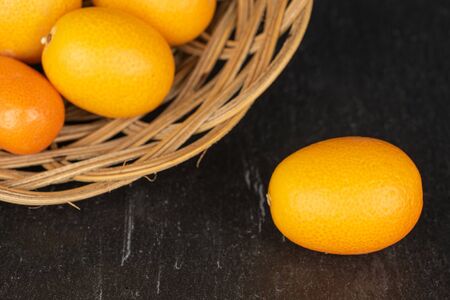 Group of five whole tasty orange kumquat in round rattan bowl on grey stoneの写真素材