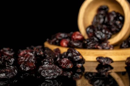 Lot of whole sweet dried cowberry																 in copper bowl on round bamboo coaster isolated on black glassの写真素材