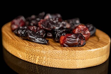 Lot of whole dried cowberry																 on round bamboo coaster isolated on black glass