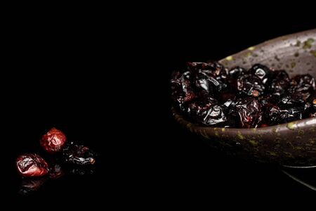 Lot of whole sweet dried cowberry																 in glazed bowl isolated on black glassの写真素材
