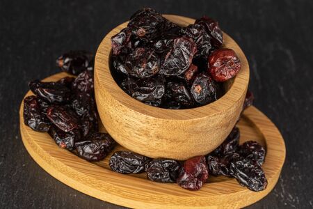 Lot of whole dried cowberry																 in bamboo bowl on round bamboo coaster on grey stoneの写真素材