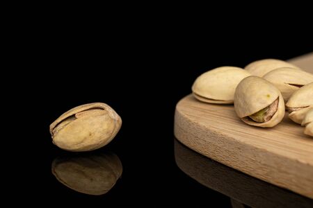 Lot of whole salted pistachio on bamboo cutting board isolated on black glass