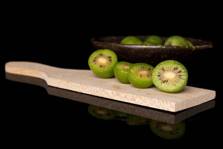 Group of lot of whole four halves of hardy green kiwi on wooden cutting board in glazed bowl isolated on black glassの写真素材