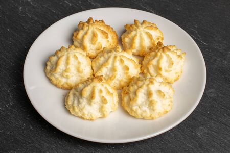 Group of seven whole homemade golden coconut biscuit on white ceramic plate on grey stoneの写真素材
