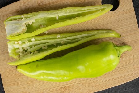 Group of one whole two halves of hot green pepper banana on bamboo cutting board flatlay on grey...