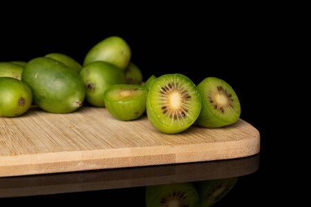 Group of lot of whole three halves of hardy green kiwi on bamboo cutting board isolated on black glassの写真素材