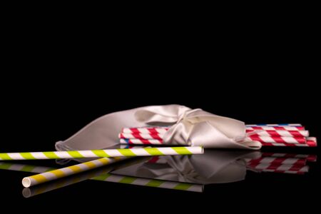 Lot of whole paper straw with white ribbon isolated on black glass