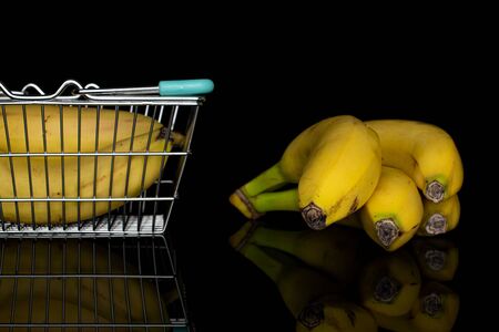Group of six whole sweet yellow banana in shopping basket isolated on black glassの写真素材