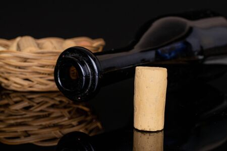 Lot of whole common wine cork  with glass bottle in round rattan bowl isolated on black glass