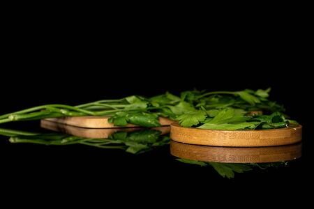 Lot of whole lot of pieces of fresh green parsley on round bamboo coaster on wooden cutting board isolated on black glassの写真素材