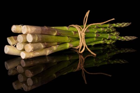 Lot of whole healthy green asparagus bunch with straw rope isolated on black glassの写真素材