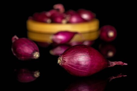 Lot of whole small red onion bulb on bamboo coaster isolated on black glass