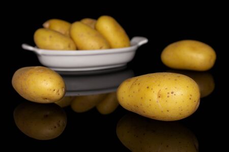 Group of eight whole pale yellow potato in white oval ceramic bowl isolated on black glassの写真素材