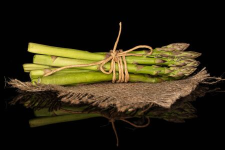 Lot of whole healthy green asparagus with straw rope and jute fabric isolated on black glassの写真素材